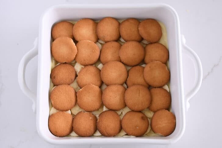 White square 8X8 baking dish with layer of vanilla pudding, sliced bananas, and nilla wafers.