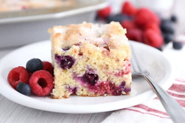 Square of cake with blueberries and raspberries on white plate.