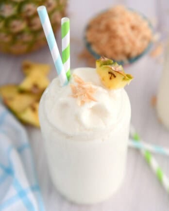 Top down view of tall glass cup with frozen piña colada, toasted coconut, a triangle of fresh pineapple and a bit of toasted coconut on top.