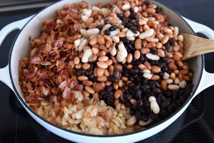 Black beans, cannellini beans, and pinto beans in cast iron pan with bacon and onions.