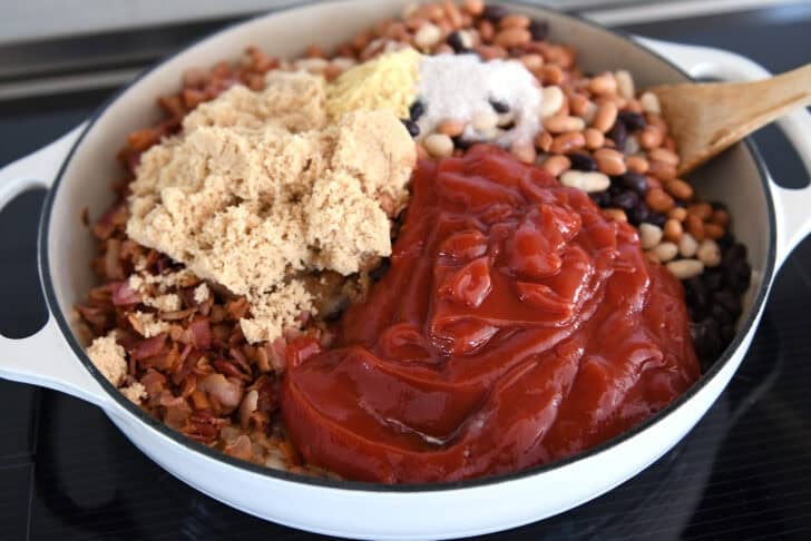Black beans, cannellini beans, and pinto beans in cast iron pan with ketchup, brown sugar, granulated sugar and dry mustard.