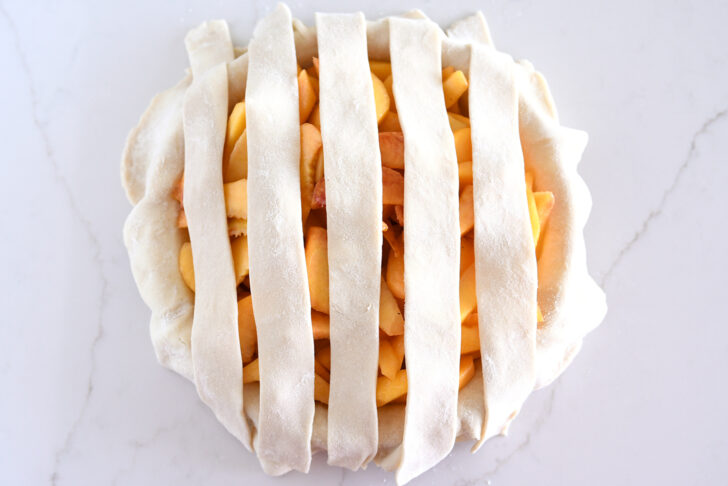 Assembling lattice pie crust on fresh peach pie.