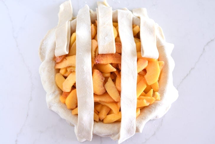 Assembling lattice pie crust on fresh peach pie.
