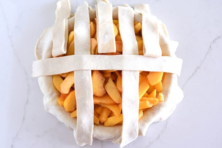 Assembling lattice pie crust on fresh peach pie.