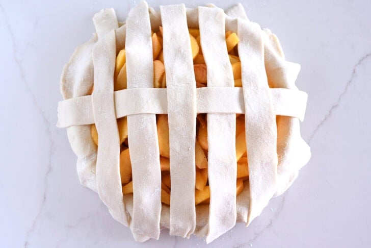 Assembling lattice pie crust on fresh peach pie.