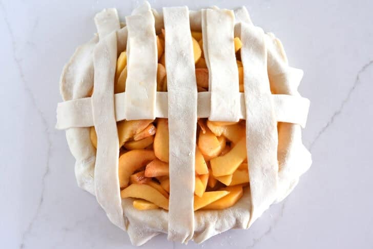 Assembling lattice pie crust on fresh peach pie.