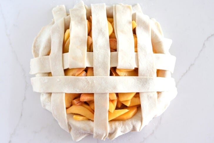 Assembling lattice pie crust on fresh peach pie.