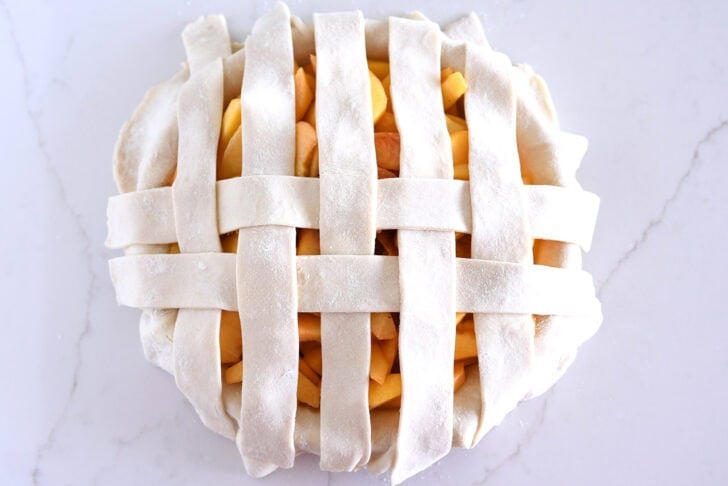 Assembling lattice pie crust on fresh peach pie.