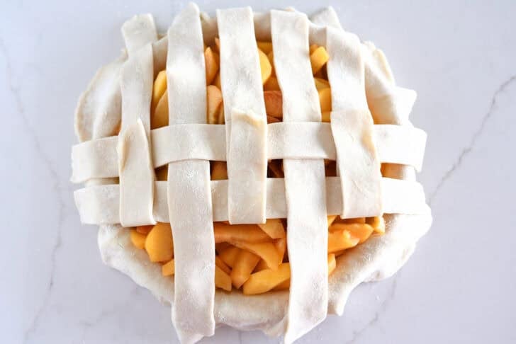 Assembling lattice pie crust on fresh peach pie.