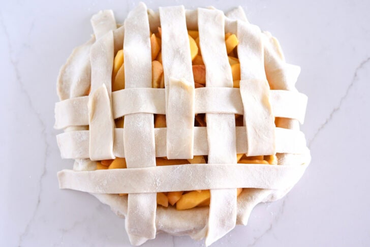 Assembling lattice pie crust on fresh peach pie.
