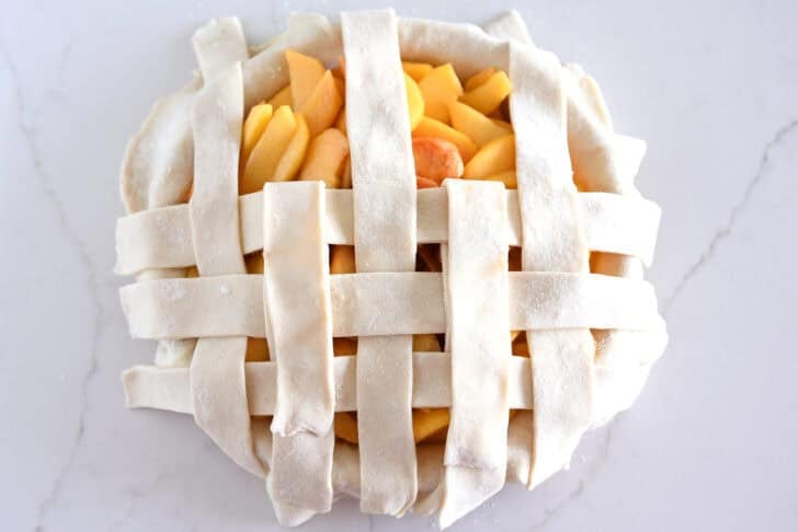 Assembling lattice pie crust on fresh peach pie.