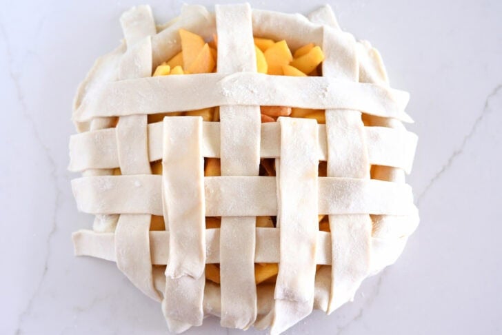 Assembling lattice pie crust on fresh peach pie.