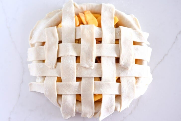 Assembling lattice pie crust on fresh peach pie.