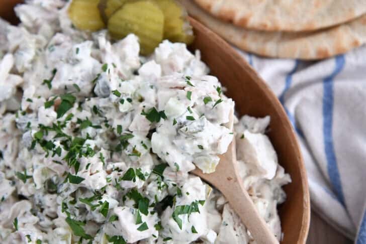 Wooden bowl filled with creamy dill pickle chicken salad with wooden spoon.