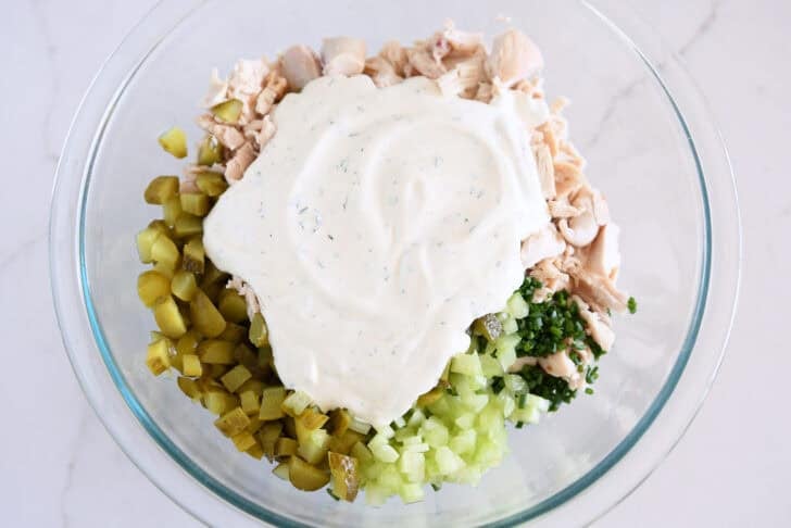 Glass bowl with celery, chopped dill pickles, green onions, chopped chicken and creamy dressing.