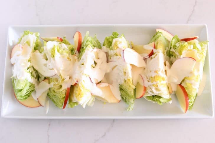 White platter with iceberg wedges, sliced apples, and blue cheese dressing.