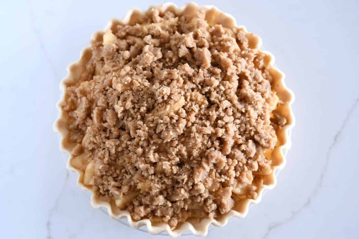 Buttery streusel on top of unbaked apples in pie crust.