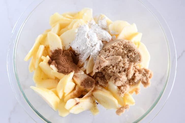 Glass bowl with sliced apples, brown sugar, flour and cinnamon.