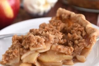 Slice of apple crumble pie on white plate with fork.