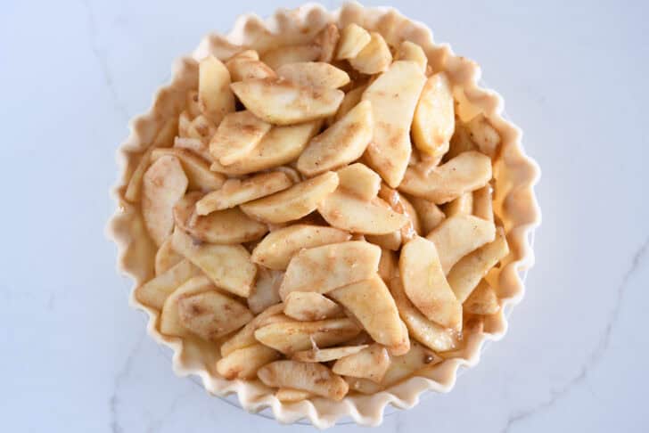 Unbaked pie crust filled with cinnamon covered apple slices.