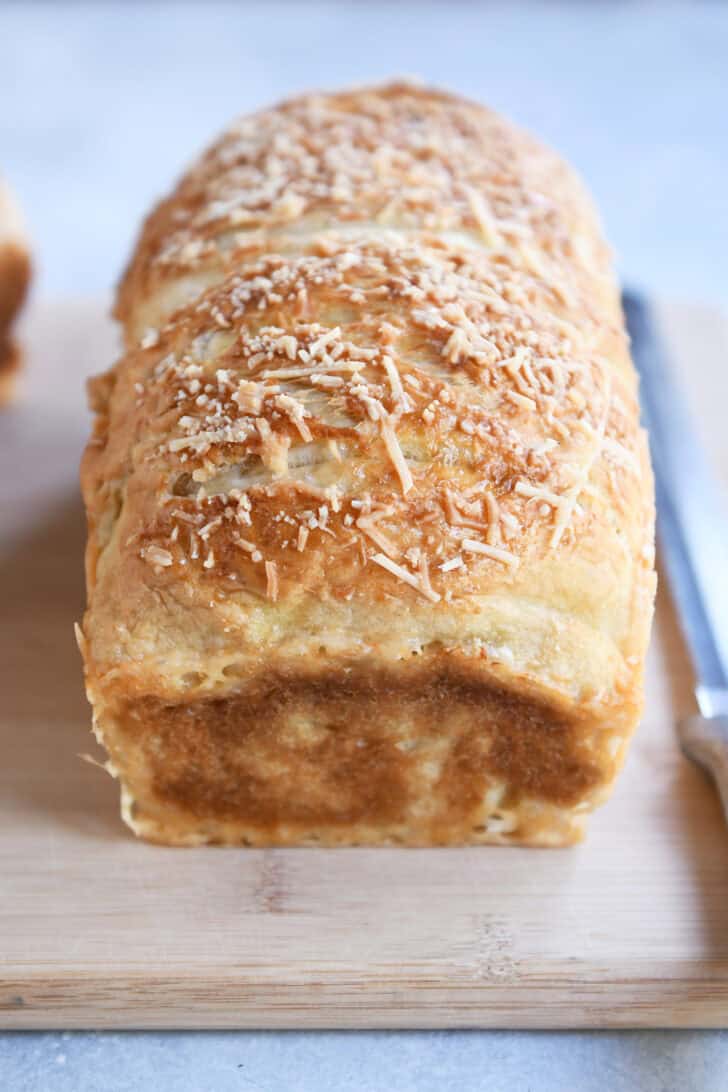 Baked loaf of bagel bread dough on wood cutting board.