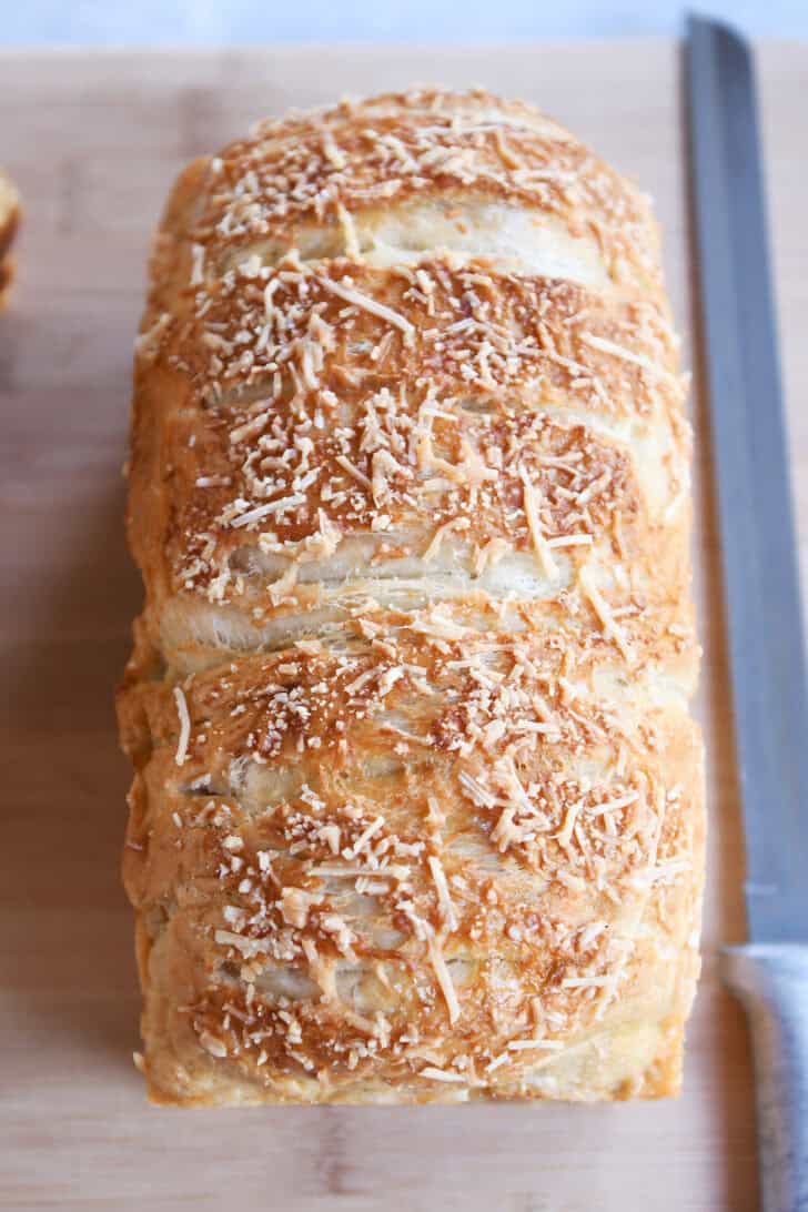 Baked loaf of bagel bread dough on wood cutting board.