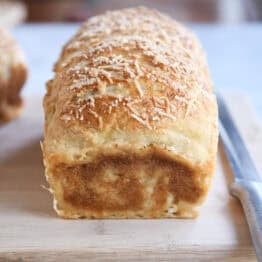 Baked loaf of bagel bread dough on wood cutting board.