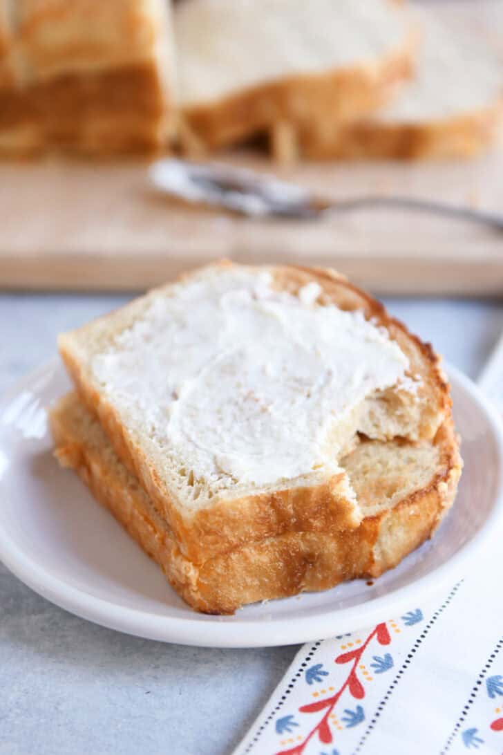 Two slices of bagel bread dough on white plate with top slice slathered with cream cheese.