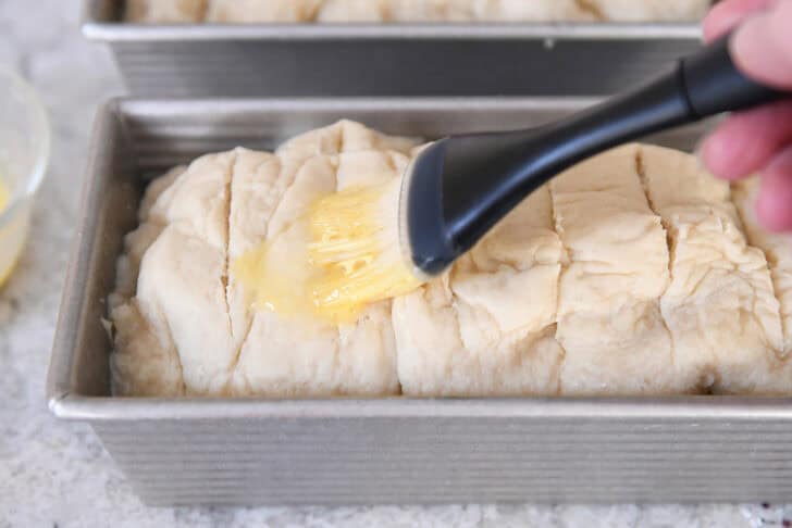 Brushing boiled loaf of bagel bread dough with egg wash.