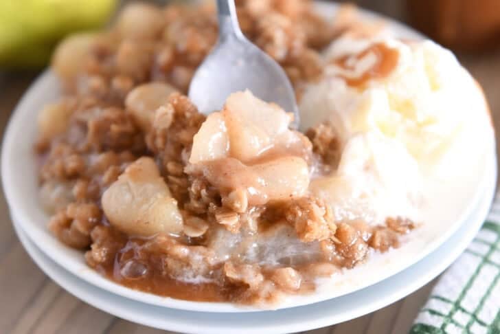 Double stack of white plates with serving of caramel pear crisp and vanilla ice cream.