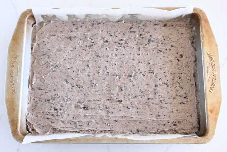 Oreo frosting spread on top of baked pan of brownies.