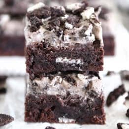Two Oreo frosted brownies stacked on white parchment paper.