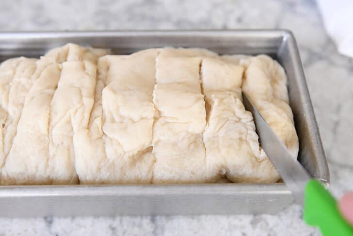 Slashing top of boiled loaf of bread dough in bread pan.