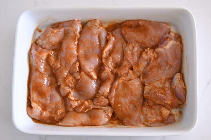 White pan with raw chicken thighs in smoky honey marinade.