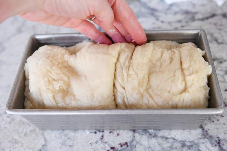 Pressing boiled loaf of bagel bread into bread pan.