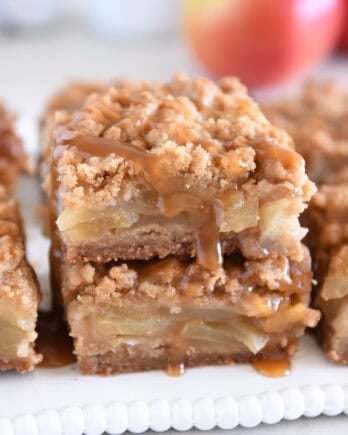 Two caramel apple crumble bars stacked on white tray.