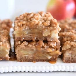 Two caramel apple crumble bars stacked on white tray.