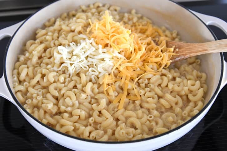 White cast iron skillet with cooked elbow macaroni, shredded cheddar, and shredded monterey jack cheese.