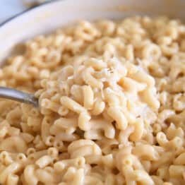 Serving spoon scooping creamy skillet macaroni and cheese.