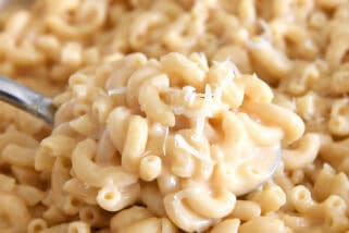 Serving spoon scooping creamy skillet macaroni and cheese.