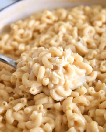 Serving spoon scooping creamy skillet macaroni and cheese.