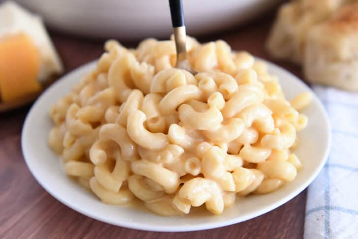 Spoon scooping bite of creamy macaroni and cheese on white plate.