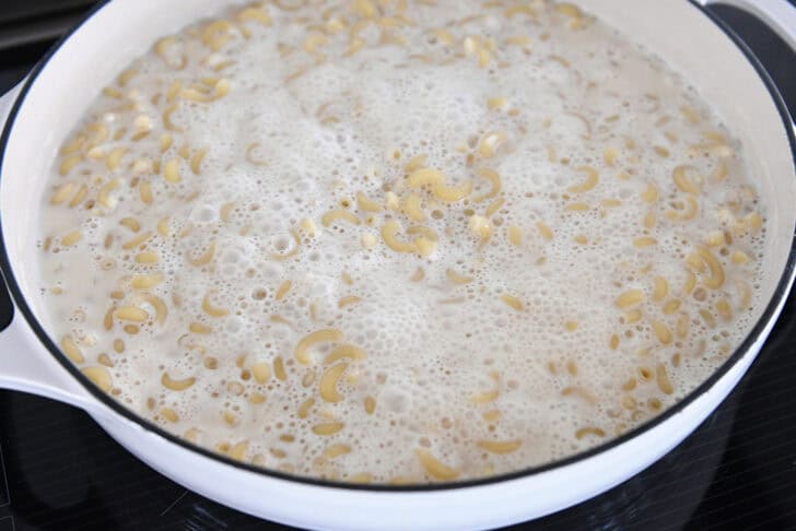 Simmering elbow macaroni in white cast iron skillet with evaporated milk and water.