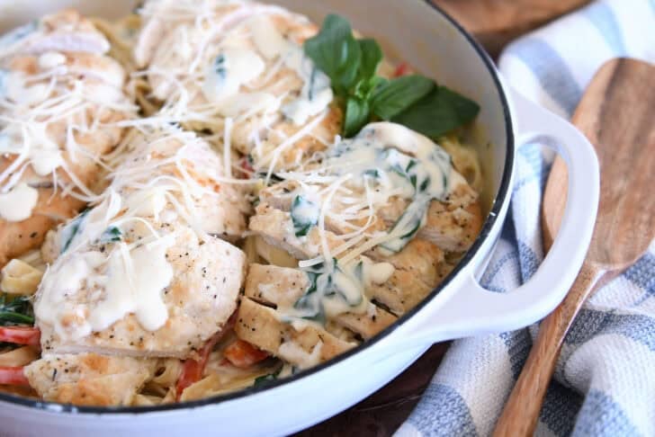 Top down view of sauteed chicken breasts on top of pasta, Parmesan cream sauce, spinach and peppers.