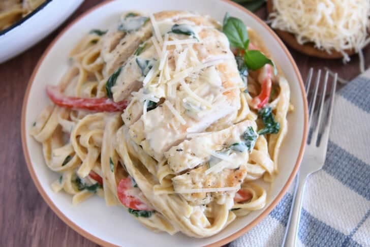 Top down view of sliced chicken breast, cream sauce, pasta, peppers and spinach.