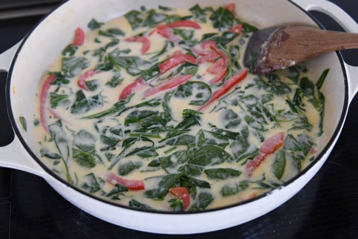 White cast iron skillet with cream sauce, spinach and peppers.