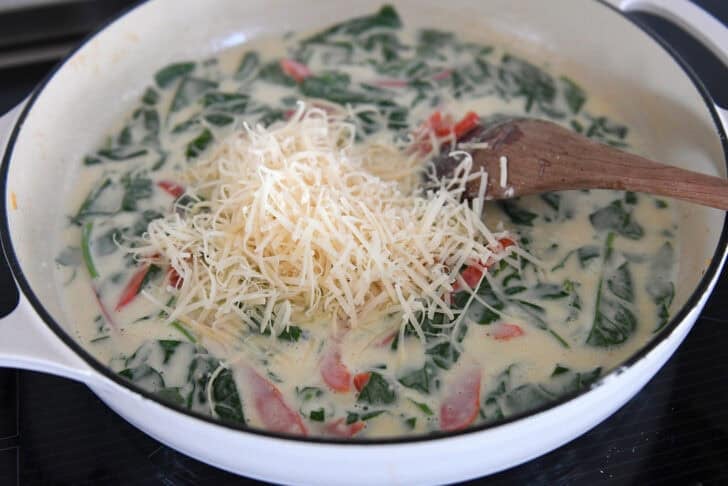 White cast iron skillet with cream sauce, spinach, Parmesan cheese, and peppers.