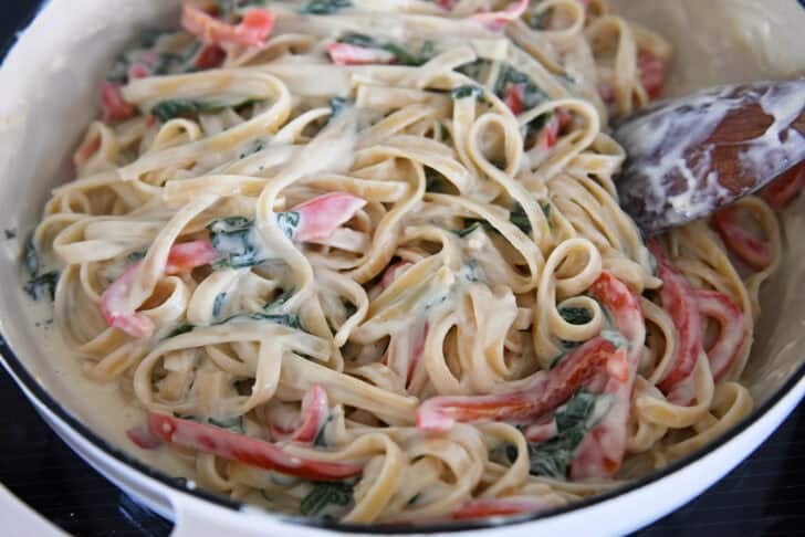 White cast iron skillet with cream sauce, spinach, Parmesan cheese, pasta, and peppers.