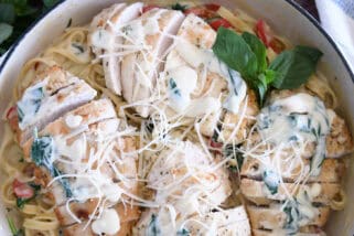 Top down view of sauteed chicken breasts on top of pasta, Parmesan cream sauce, spinach and peppers.