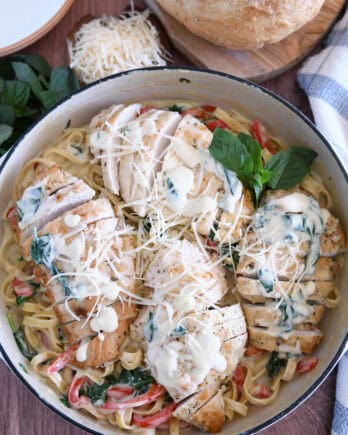 Top down view of sauteed chicken breasts on top of pasta, Parmesan cream sauce, spinach and peppers.